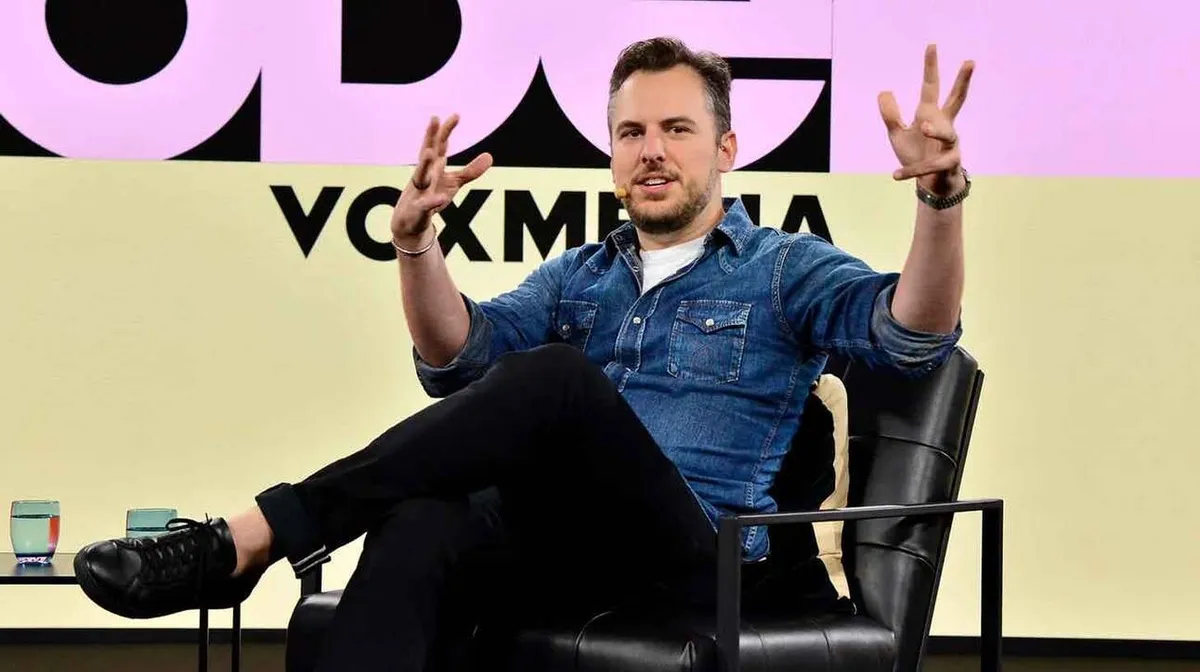 Mees istub mustal toolil, kandes teksasärki ja musti pükse. Ta räägib käed liigutamisega. Taustal on tekst 'VOX MEDIA'. Vasakul esiplaanil on kaks klaasi veega.
