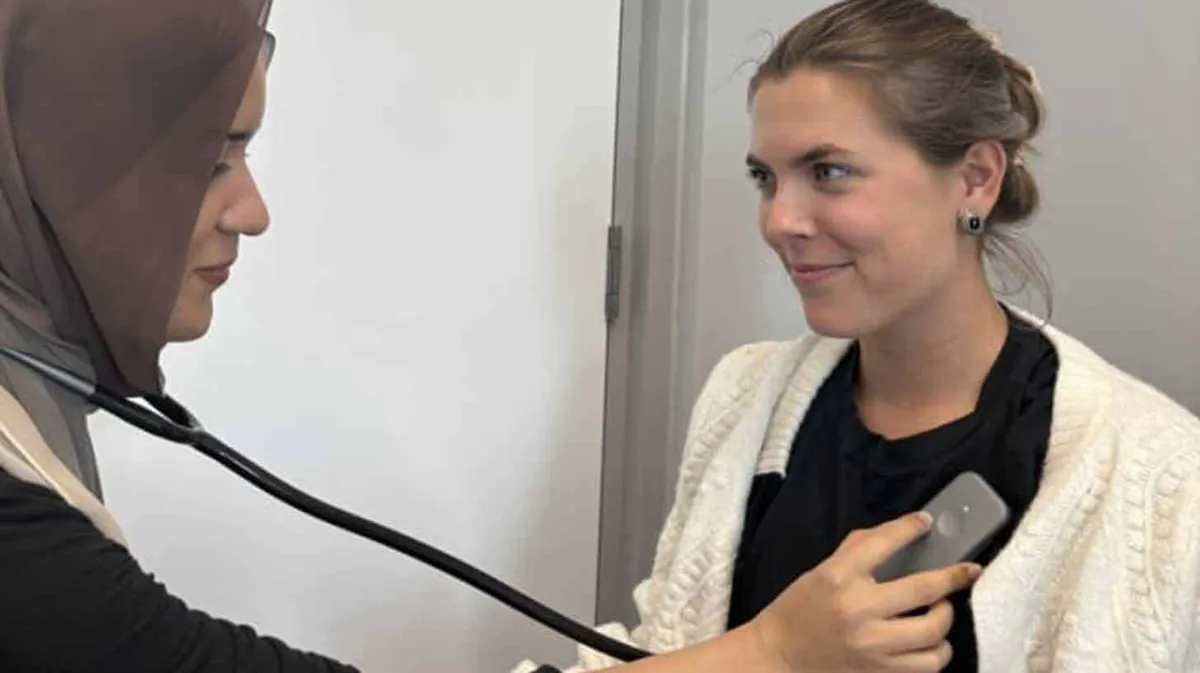 Kaks naist, üks kannab pead loorituna ja kasutab stetoskoopi teise naise südame kuulamiseks. Teine naine naeratab ja kannab valget kampsunit.