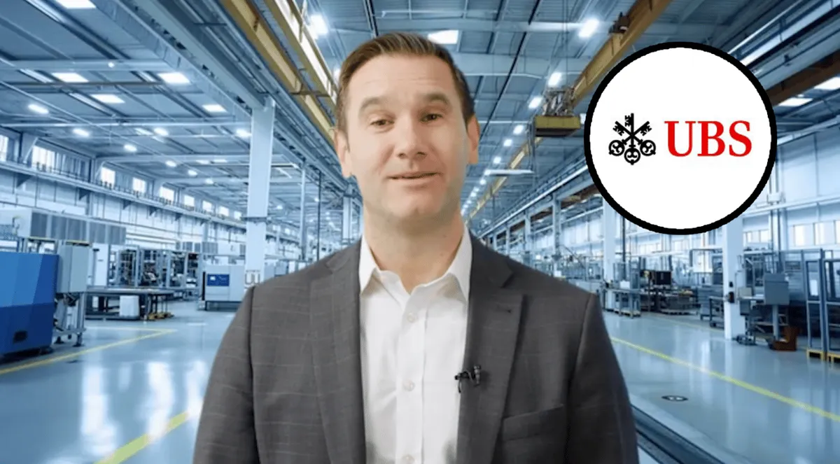 Säravkollane valgusküllane tööstushoone, mille ees seisab mees mustas ülikonnas. Paremal ülanurgas on UBS-i logo.
